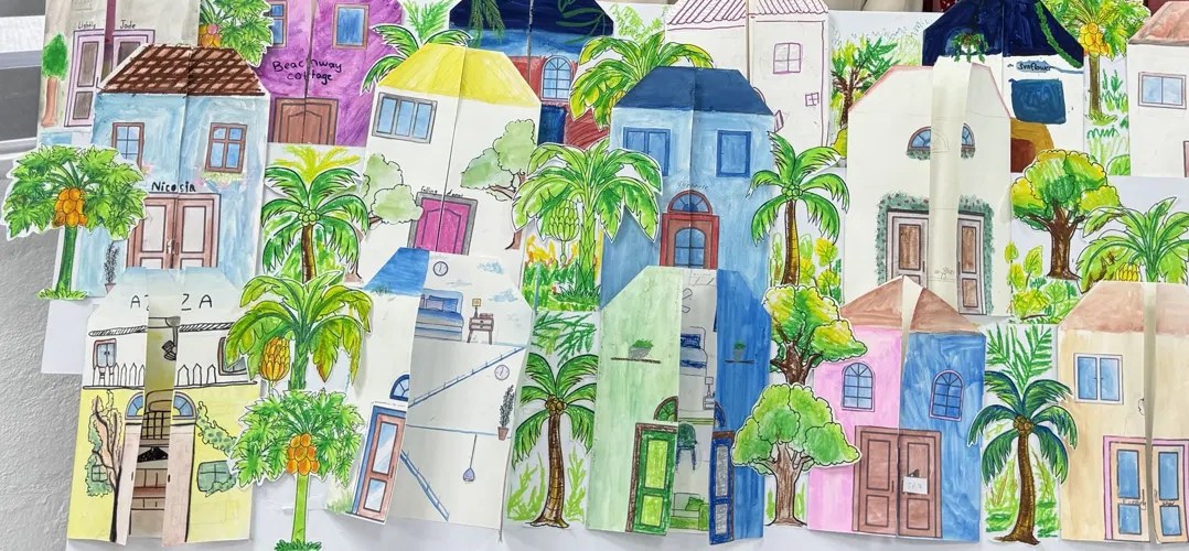A wall-sized street of brightly hand-drawn paper houses and palm trees, made by students